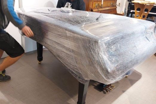 Der verkaufte Flügel wird zum Schutz über den zuvor gelegten Decken gut in Folie verpackt. Im Ausstellungsraum von Piano Fies, Oberkirch